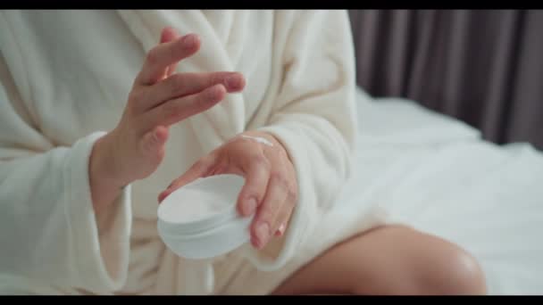 一个穿着浴衣的女人正坐在床上 用自己的双手按摩奶油 她的手腕和大姆指上有一种温和而舒缓的姿势 — 图库视频影像