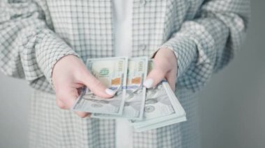 Moda desenli ceketli bir iş kadınını titizlikle ABD dolarlarını sayarken gösteren yakın plan bir resim.