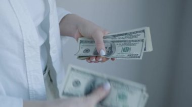 Finansal işlemleri ve nakit yönetimini vurgulayan 100 dolarlık banknotlar sunan bir kadının ellerini gösteren net bir görüntü.