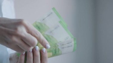 Görüntü, 100 Euro 'luk banknotları yakından inceleyen bir kadını gösteriyor. Para biriminin güvenilirliğini sağlamak için güvenlik özelliklerine odaklanıyor.
