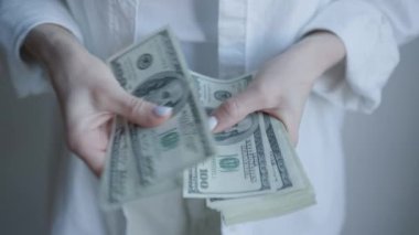 Amerikan dolarlarını sayarken, kişisel mali yönetim ve günlük para idaresini vurgulayan bir kadının ellerini tasvir ediyor.
