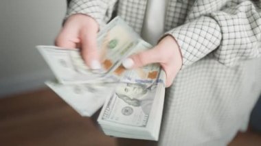 Ekose takım elbiseli bir kadın, kişisel mali yönetim ve nakit işleme resmedilmiş bir yığın ABD doları banknotlarına bakıyor.