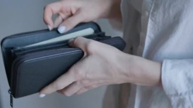 Bu görüntü, bir kadının siyah deri bir cüzdandan Amerikan doları çekerken ellerini yakalıyor ve günlük hayatta rutin bir finansal işlemin altını çiziyor.