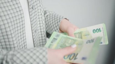 Bu görüntü, profesyonel bir kadının ellerini çok dikkatli bir şekilde tutarken, zarif bir ceketle kaplanmış, finansal yönetimi ön plana çıkaran ve...