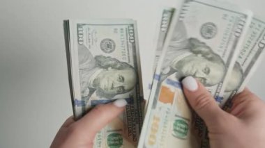 Zenginlik, finansal işlemler ve ekonomik faaliyet temalarını yansıtan, titizlikle bir yığın 100 dolarlık banknotları sayarken el ele çeken yakın plan bir görüntü.
