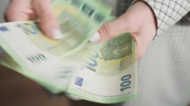 Bir iş kadınının 100 Euro 'luk banknotları hızla sayarken el ele tutuşması, akışkan hareket ve finansal işleme uzmanlığını yakalaması.