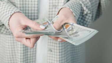 Büyük miktarda Amerikan doları sayarken, finansal anlaşmaları ve zenginlik yönetimini ön plana çıkaran bir iş kadınının ellerine yakından bakın.
