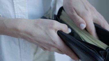 Resim, 100 dolarlık banknotları siyah bir cüzdana yerleştirirken, tasarruf, mali güvenlik ve nakit işlemleri temaları vurgulanıyor