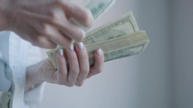 Bir kadının elleri, zenginlik, finans ve manuel para işleme kavramlarını vurgulayan, kalın bir yığın 100 dolarlık banknotları sayarken görülüyor.