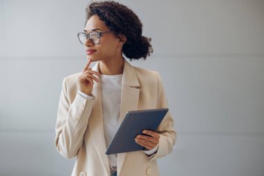 Modern ofis arka planında duran dijital tabletli güzel bir bayan yönetici. 