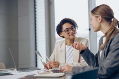 Projede birlikte çalışan iki odaklanmış kadın iş arkadaşı ofiste dizüstü bilgisayar kullanıyor.