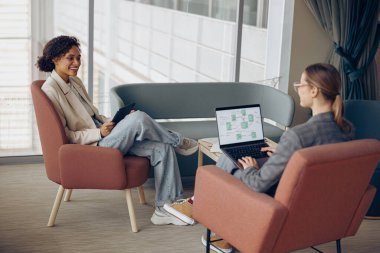 Yeni projede birlikte çalışan kadın yöneticiler ve ofiste oturan dizüstü bilgisayar ve dijital tablet kullanıyorlar