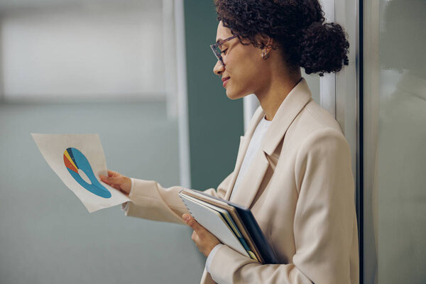 Pretty Female Entrepreneur Looking Financial Documents While Standing Office Background Stock Photo