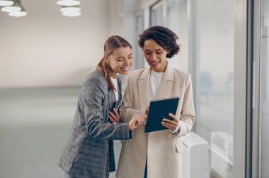 Gülümseyen kadın iş adamları modern birlikte çalışıp dijital tablet kullanıyorlar.