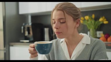 Bir kadın modern mutfağında kahve molası veriyor, iş günü ortasında bir dinlenme ve tefekkür anı yakalıyor. Sahne gençleşmek için ara vermenin önemini vurguluyor..