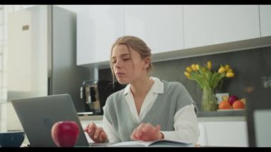 Genç bir kadın, bir kitap okurken modern mutfağından uzaktan çalışırken görülüyor. Odaklanması ve üretkenliğe olan bağlılığını vurguluyor. Şık ve düzenli mutfak mükemmel bir zemin oluşturur.