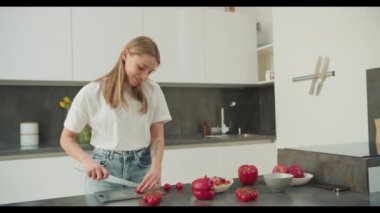 Odaklanmış genç bir kadın mutfak tezgahında dolma biber ve domates kesiyor, çağdaş bir mutfak ortamında canlı ve sağlıklı bir salata yapıyor..