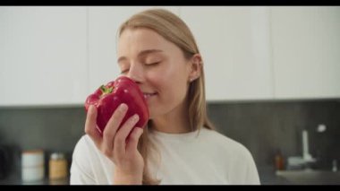 Kırmızı dolmalık biberi zevkle koklayan genç bir kadını yakın plan çekimde yakalar. Tarz sahibi mutfağında yemek hazırlarken tazeliğini takdir eder.