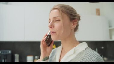 Modern bir mutfakta genç bir kadın telefonda konuşurken gülümsüyor. Bu görüntü, çağdaş bir ev ortamında, teknolojiyi ve kişisel yaşamı ön plana çıkaran olumlu bir iletişim anı yakalar.
