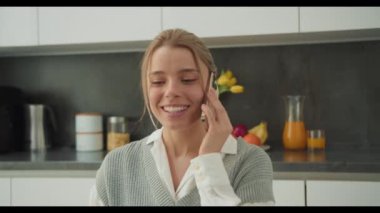 Modern bir mutfak ortamında akıllı telefondan konuşan genç bir kadın. Meşgul ve neşeli görünüyor. Canlı ve verimli bir uzaktan çalışma ortamı sağlıyor. Profesyonel ve ev hayatını dengeliyor.