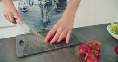 Genç bir kadın modern bir mutfakta yeni kesilmiş domatesleri dilimliyor. Marul ve domates gibi diğer sebzelerle birlikte sağlıklı bir yemek hazırlarken, resim ellerini yakalıyor.
