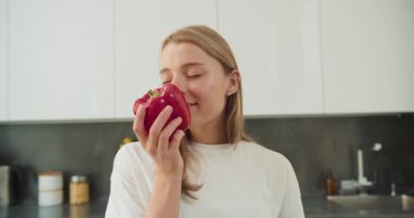 Genç bir kadın yüzüne kırmızı bir dolma biber tutarak taze, doğal kokusundan zevk alırken gözleri kapalı gülümsüyor. Sahne, minimalist tasarımı olan modern bir mutfakta geçiyor.