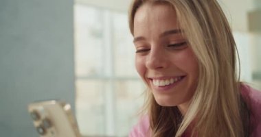 Video çekimi sırasında içten bir şekilde gülümseyen gerçek mutluluk ve nişanı gösteren bir kadının yakın çekimi. Sahne, parlak bir ortamda dijital bağlantı ve iletişimi vurguluyor.