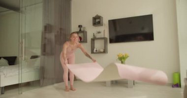 Bir kadın egzersiz minderini modern bir oturma odasına yerleştirir, antrenman seansına hazırlanır. Açık renkli etek giyiyor, sağlıklı bir yaşam tarzına bağlılığını vurguluyor..