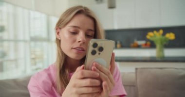 Genç bir kadın kanepede rahat bir şekilde uzanıyor, akıllı telefonunu yüzüne doğrultuyor. İçerikte ilerlerken odaklanmış ve rahat görünüyor, rahat ve rahat bir atmosfer yaratıyor..