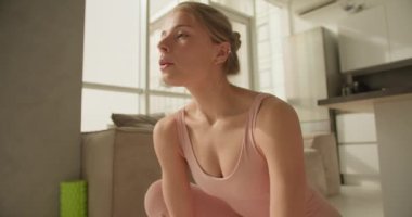 Pembe yoga kıyafetli neşeli bir kadın, parlak bir mutfakta sıcak bir şekilde gülümser, yoga seansından sonra pozitiflik ve rahatlama yayar, farkındalık ve öz bakım anı yakalar..