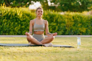 Bir kadın, doğanın ferahlatıcı yeşiliyle çevrili bir şekilde, dışarıda yoga meditasyonu yapıyor.