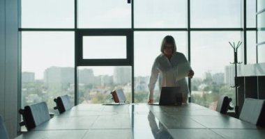 Bir iş kadını, parlak, modern bir ofisteki, yerden tavana pencereli, şehir manzaralı, somutlaştırıcı odak ve profesyonelliği olan şık bir konferans masasında önemli belgeleri inceliyor..