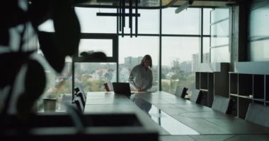 Profesyonel bir iş kadını, şehir siluetini gösteren geniş pencereli çağdaş bir konferans odasında şirket liderliğini ve stratejik planlamayı sembolize eden belgeleri incelerken görülüyor..