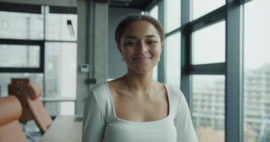 Zarif bir ofiste gülümseyen kendine güvenen genç bir kadın modern dekor ve geniş pencerelerle profesyonelliği, güçlendirmeyi ve yaratıcılığı somutlaştırıyor. Doğal ışık onun odaklanmış ve pozitif olduğunu vurguluyor.