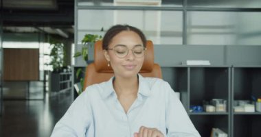 Gözlüklü genç bir kadın, dizüstü bilgisayarını raflar, bitkiler ve doğal ışıklandırmanın yer aldığı modern, iyi tasarlanmış bir ofis alanında kapatıyor ve odak ve üretkenlik anı yakalıyor.