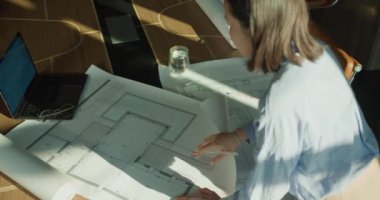 Yukarıdan çekilmiş modern bir çalışma alanı, bir mimarın dizüstü bilgisayar, bardak ve su gibi araçları dikkatlice inceleyerek yaratıcılığı ve odaklanmayı vurguluyor..