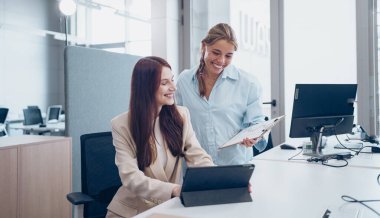 İki başarılı profesyonel kadın modern bir ofiste dijital cihazlar kullanarak odaklanmış bir tartışmaya girişiyor.