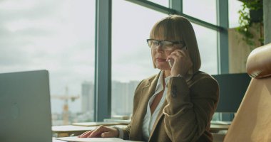 Modern ofis ortamında profesyonel bir kadın şehir manzarası ile telefonda iş konuşuyor. Yüksek kalite fotoğraf