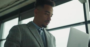 Kareli takım elbiseli profesyonel bir işadamı şık bir ofiste dizüstü bilgisayar üzerinde çalışıyor. Modern çevre ve doğal ışıklandırma profesyonel ortamı geliştirir. Yüksek kalite 4k