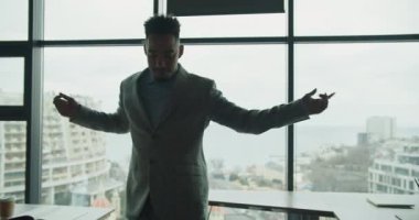 Şık takım elbiseli bir işadamı, geniş pencereli ve şehir manzaralı modern bir ofiste neşeyle dans ederken görülüyor. Neşeli bir kutlama ve enerji anı. Yüksek kalite 4k görüntü