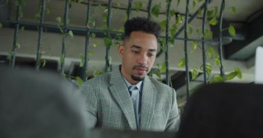 Kareli takım elbiseli düşünceli bir işadamı modern bir ofisteki belgeleri analiz ediyor. Yeşil bitkiler ve gösterişli dekorlar sakin ve profesyonel bir atmosfer yaratıyor. Yüksek kalite 4k görüntü