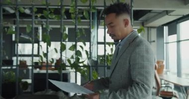 Odaklanmış bir profesyonel, yeşillik dolu modern ve şık bir ofiste mimari belgeleri inceliyor. Sahne yaratıcılık, profesyonellik ve yenilik yayar. Yüksek kalite 4k görüntü