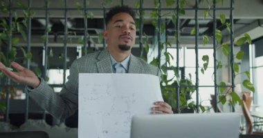 Modern bir çalışma alanında kendinden emin ve çekici bir profesyonel online bir toplantı sırasında ayrıntılı bir kat planı sunar. Arka planda yemyeşil, taze bir dokunuş var. Yüksek kalite 4k