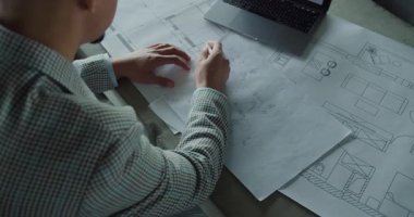 Bir mimarın ellerinin, bir çalışma alanının detaylı teknik planlarını analiz etmesi ve notlaması. Görüntü kesinliği, yaratıcılığı ve profesyonel tasarım süreçlerini vurgular. Yüksek kalite 4k