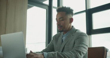 Şık, modern bir ofiste dizüstü bilgisayarda yazı yazan ve şehrin ufuk çizgisini gören profesyonel bir işadamı. Yüksek kalite 4k görüntü