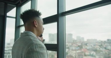 Ekose takım elbiseli profesyonel bir işadamının geniş bir pencerenin yanında dikilip, arka planda bulanık bir ufuk çizgisi olan telefonla konuşmasının yan görüntüsü. Yüksek kalite 4k görüntü