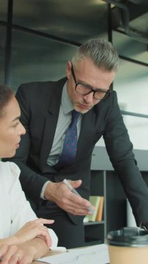 İş adamı, modern bir ofiste oturan bir iş kadınına bir rapor sunuyor. Takım iletişimi ve strateji planlaması devam ediyor.
