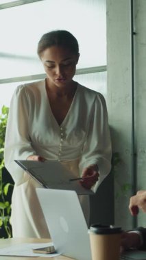 Kendine güvenen bir iş kadını modern bir ofiste dizüstü bilgisayarda çalışan bir iş adamına belgeler gösterir. Takım çalışması, iletişim ve kurumsal karar verme kavramı.