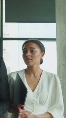 Bir işadamı ve işkadını, elinde belge ve dosya tutarken modern bir ofiste yürüyorlar. İşle ilgili görevleri tartışıyor ya da toplantıya hazırlanıyor gibi görünüyorlar..