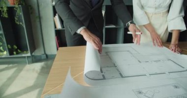 İş adamı ve iş kadını modern bir ofiste bir masada mimari planlar üzerinde işbirliği yapıyor, planlama oturumunda planı ve ayrıntıları tartışıyor..